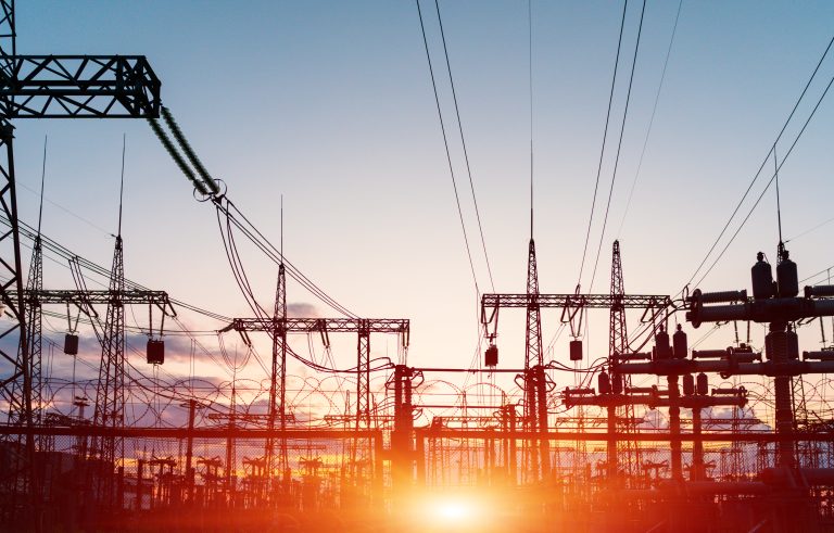 Voimalaitoksen sähkölinjoja auringonnousun värjäämässä maisemassa