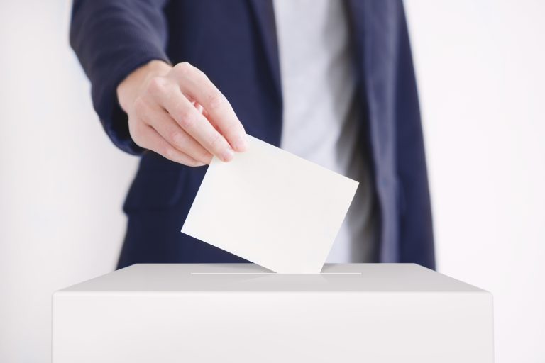 Pukuun pukeutunut henkilö laittaa äänestyslippua vaaliuurnaan.