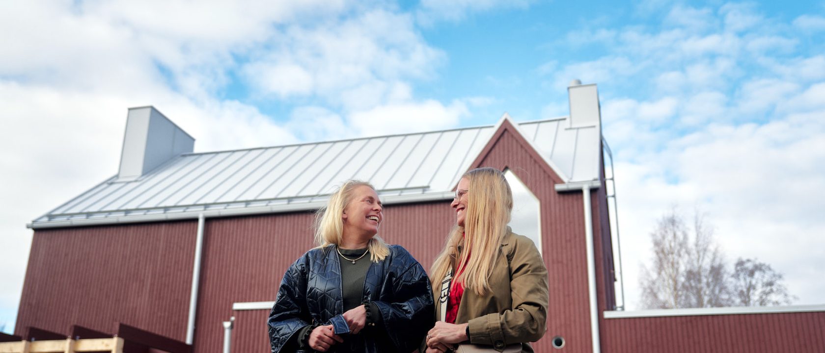 Hanna Luukkonen (vas.) ja Riikka Säkkinen katsovat toisiaan hymyillen punaisen talon edessä.