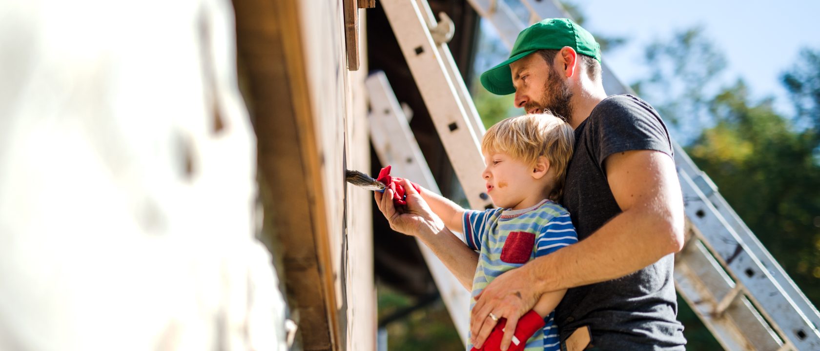 Isä ja lapsi maalaamassa taloa aurinkoisena päivänä