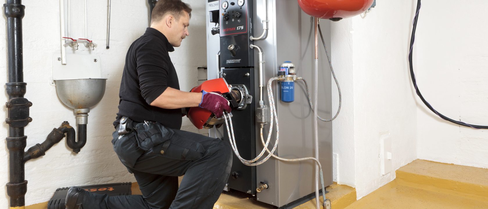 Nuori mies huoltaa omakotitalon öljylämmityslaitteistoa.