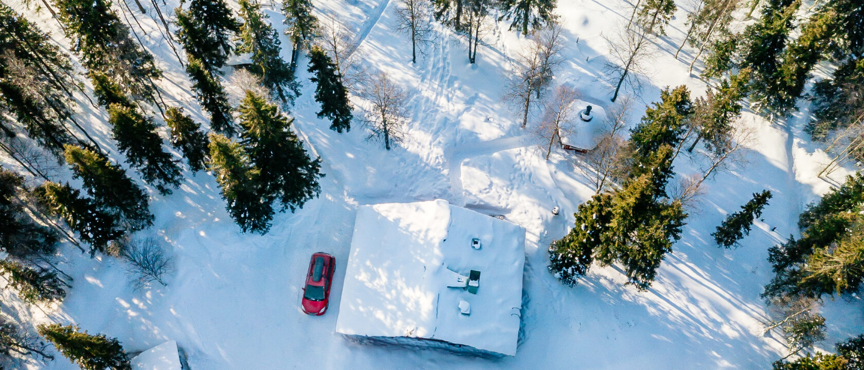 Ilmakuva talosta talvisen metsän keskellä järven rannalla.