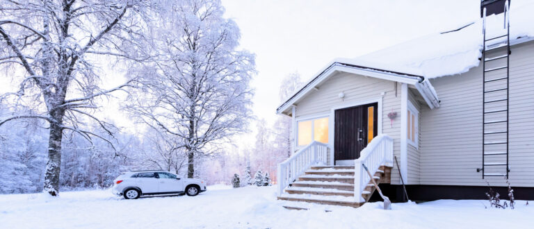 Vaalea puutalo lumisessa maisemassa