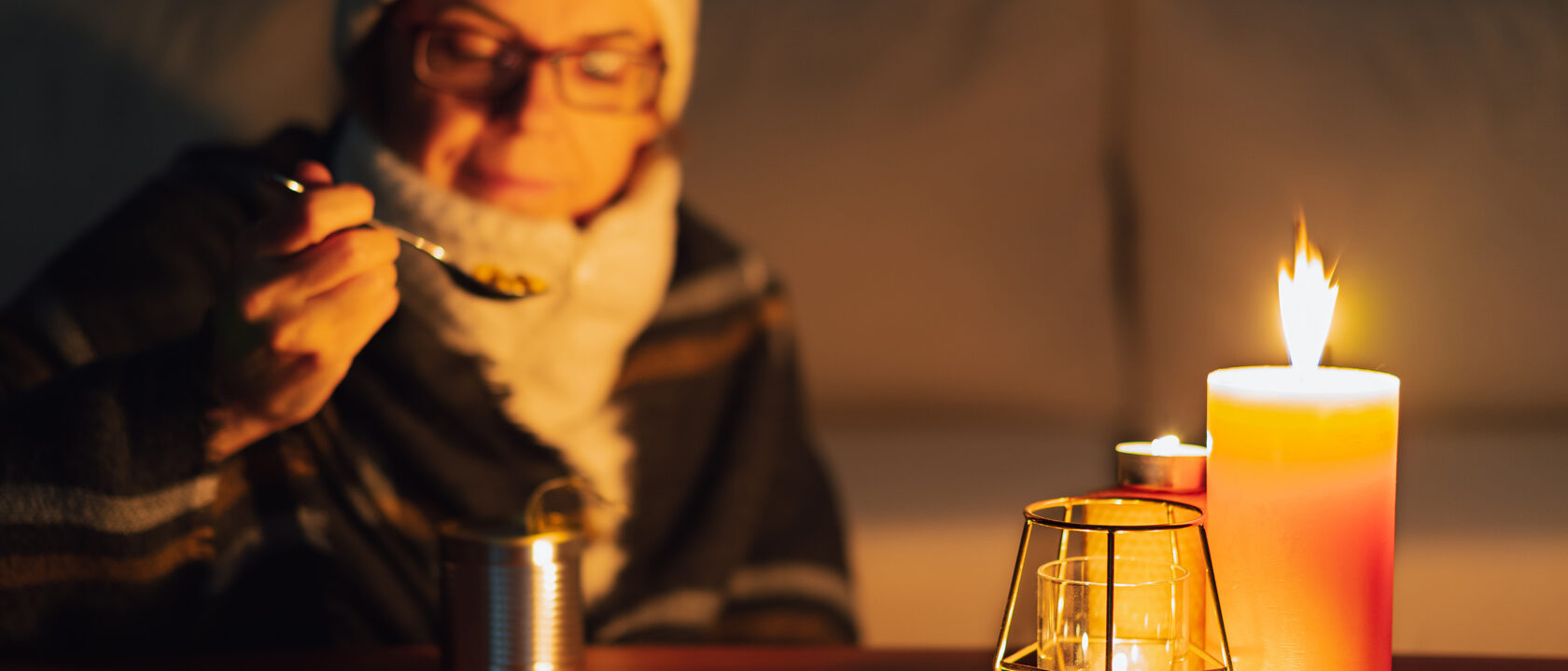 Lämpimästi pukeutunut ihminen syö retkiruokaa kynttilänvalossa